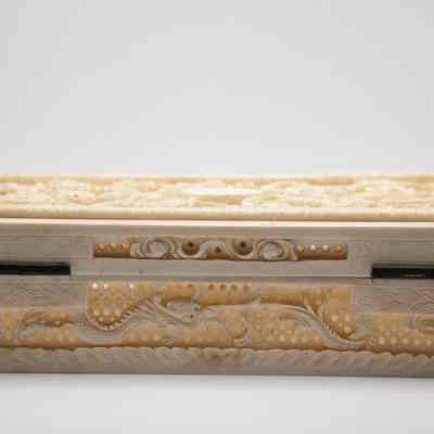 Back of the carved ivory dragon box from India.: Image of the back of rectangular ivory box. It is debossed with a dragon and there are carved holes.