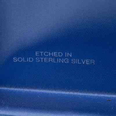 Image of the official stamp on the inside of the box.: Image of silver writing on the inside of the blue satin lid, reads "ETECHED IN SOLID STERLING SILVER."