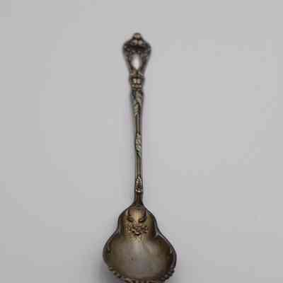 Spoon: The image shows an ornately designed, vintage silver spoon on a plain background.