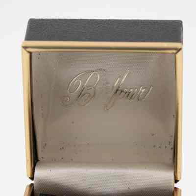 Inside of L.T. Jordan's 1929 class ring from Texas A&M University box.: Up close image of the inside of L.T.'s ring box. The box is black with gold trim and has a white satin inside. The company name, "Balfour," is written in gold cursive on the inside of the lid of the box.