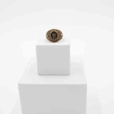 L.T. Jordan's 1929 class ring from Texas A&M University.: Image of L.T.'s ring sitting on a white block. L.T.'s class ring is gold with eagle and shield on the front. There is an embossed "29" under the shield, representing his class year. Around the center it reads "A&M COLLEGE OF TEXAS." The ring is in what is known as the "antique" style, with black coloring in the grooves of the gold.