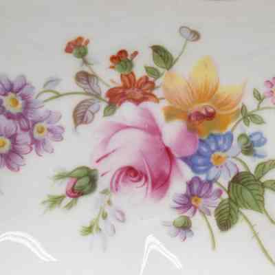 Middle of the Royal Crown Derby cigarette box lid.: Up close image of the center of the cigarette box lid. The ashtray is white bone China and decorated with yellow, pink, blue, purple, and red flowers with green leaves. There is also a gold foil detail around the outside.