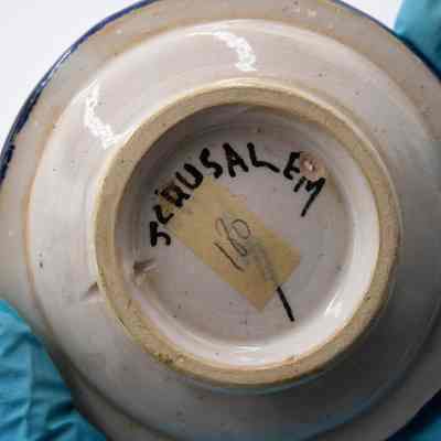 Bottom of one of the ceramic ashtrays given to the Jordans by a ruler in Bombay.: Up close image of the bottom of one of the ceramic ashtrays. It is painted with "JERUSALEM" and the artist signature. Additionally there is a piece of yellow masking tape with the number "180" written on it.