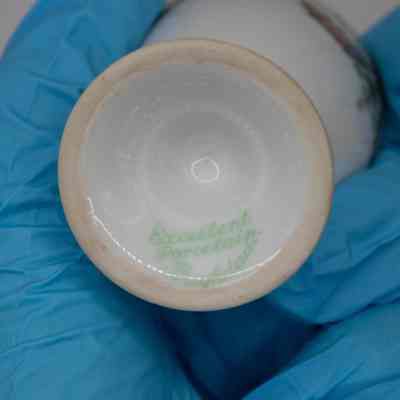 Bottom of egg cup: Solid white with green cursive reading, "Excellent porcelain, Baghdad."