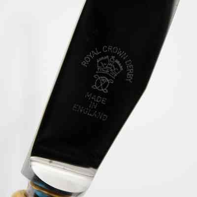 Makers mark on Royal Crown Derby knife.: Up close image of the silver blade of the knife with an engraved makers mark. The mark reads "ROYAL CROWN DERBY" on top of a small crown with "MADE IN ENGLAND" on the bottom.