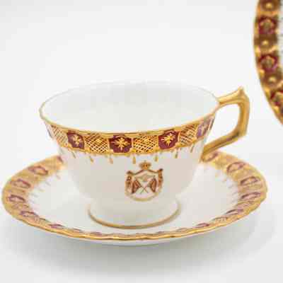 Matching Royal Crown Derby China teacup and saucer.: Image of the white bone China teacup and saucer decorated with gold and red border with Kuwaiti royal seal in middle. The handle and rim of the teacup is also decorated in gold.