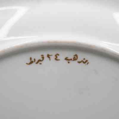 Back of the Royal Crown Derby China plate.: Up close image of stamped gold Arabic script on the back of the white China plate.