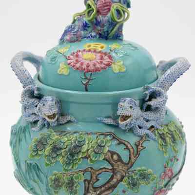 Front of the turquoise Chinese footed incense burner from Hong Kong.: Up close image of the turquoise incense burner decorated with a Chinese elm tree, pink lotus flowers, and three blue dragons. The burner has three legs that are pink with faces.