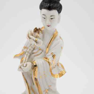 White and gold porcelain Guanyin figurine.: Up close image of a white porcelain figurine of a woman holding a flower with gold trim and black hair.