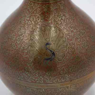 Peacock urn: The tall brass urn features intricate red floral designs and a peacock motif.