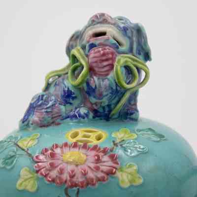 Lid of the turquoise Chinese footed incense burner from Hong Kong.: Up close image of the lid of the turquoise incense burner. It is decorated with a pink lotus flower, green leaves, and a blue dragon.