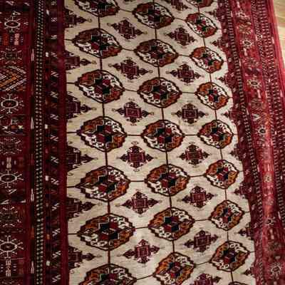 Red prayer rug: The red prayer rug features intricate geometric patterns with tan fringe along the edges.