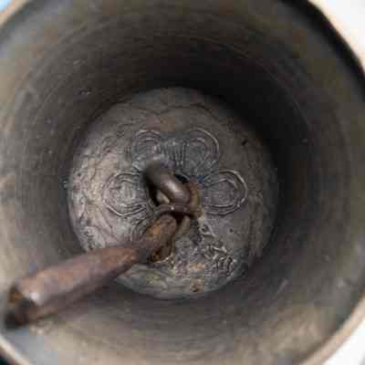 Inside of bell: The image shows the interior of a brass Tibetan ritual prayer bell featuring intricate designs at the base and a rusted clapper suspended inside.