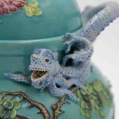 Handle of the turquoise Chinese footed incense burner.: Up close image of one of the handles on the turquoise incense burner. It is shaped like a blue dragon. There is also a Chinese elm tree.