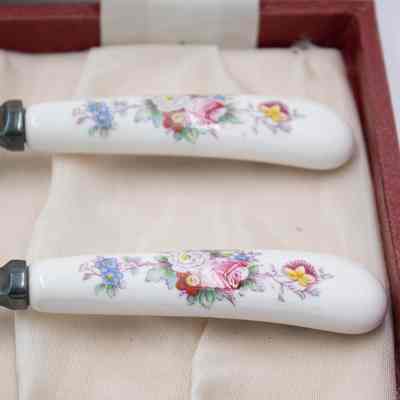 The bone China handles of the Royal Crown Derby silver salad spoons. They have a floral pattern printed on them.: Up close image of the bone China handles of the salad spoons. They are white and have blue, yellow, pink, and red flowers with green leaves printed on them.
