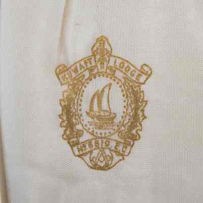 Kuwait Masonic Lodge 6810 seal on the inside of the lid of the spoon case.: Up close image of the Kuwait Masonic Lodge 6810 seal stamped in gold on the white fabric. The seal reads "KUWAIT LODGE No. 6810 E.C." and has a Kuwaiti dhow in the center. There is also the traditional Masonic compass at the bottom of the seal and two branches around the outside.