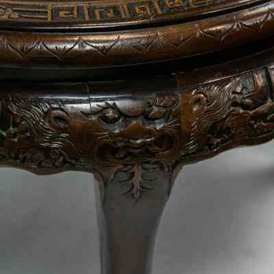 Round carved Hong Kong table legs: The intricately carved Hong Kong table features ornate details under its round glass top.