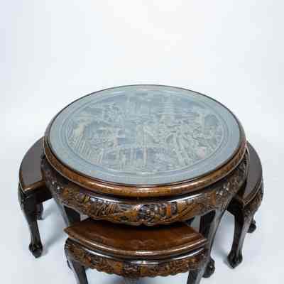 Round carved Hong Kong table and stools: The image features a round carved Hong Kong wooden table with intricate designs, complete with a glass top and matching curved stools underneath.