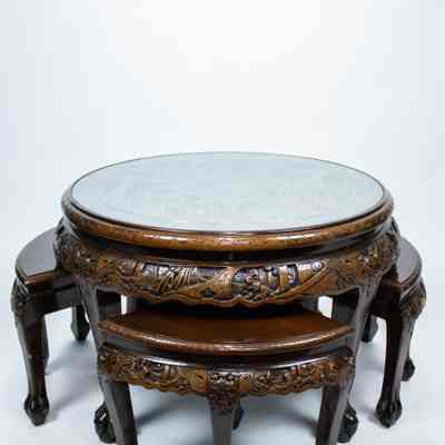 Round carved Hong Kong table and stools: A round Hong Kong table features intricate carvings and a glass top, accompanied by matching stools fitting seamlessly underneath.