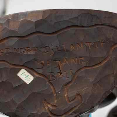 Bottom of the carved wooden figurine from Bali.: Up close image of the bottom of the carved wooden figurine. It is carved with the words "IGST. NGRH/ DjELANTIK SEDANG, BALI."