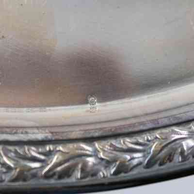 Maker Stamp: Close-up image of the silver tray. There is a small physical stamp on the outside rim, a few upright C's overlaid upon each other.