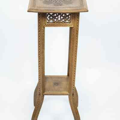 Tall table: The intricately carved, square wooden table features a detailed, light brown finish, showcasing elaborate patterns.