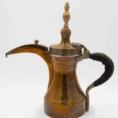 Brass and copper coffee pot: A copper coffee pot with leather-wrapped handle, brass details, and stamped Arabic script.