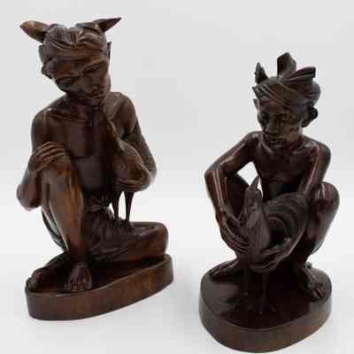 Pair of carved wooden figurines from Bali.: Image of the pair of carved wooden seated cockfighters with cock figurines.