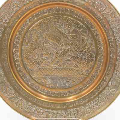 Brass acrobat plate: A medium sized plate with engravings of floral patterns around the central figures. One is an acrobat, one plays an oud, and the other fans themself.
