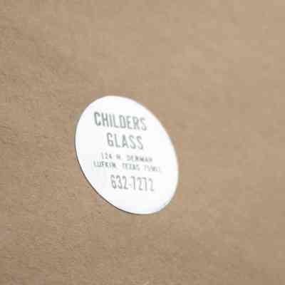 Frame Maker: Image of the frame's wooden back with a silver sticker. The sticker reads in black capital letters "Childers Glass 124 W. Denman Lufkin, Texas 75901 632-7272."