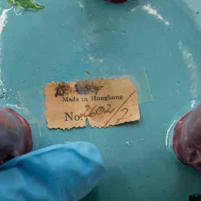 Bottom of the turquoise Chinese footed incense burner from Hong Kong.: Up close image of the bottom of the turquoise incense burner. There is a yellowed piece of paper that reads "Made in Hongkong No. 2602/2" and is taped on.