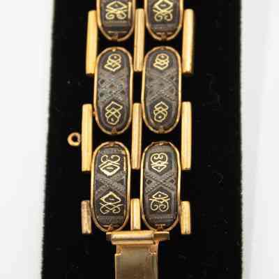 Design on gold Egyptian bracelet given to Mrs. Jessie Jordan by King Farouk I of Egypt.: Up close image of the gold bracelet with two rows of Egyptian-style designs on black bracelet display.