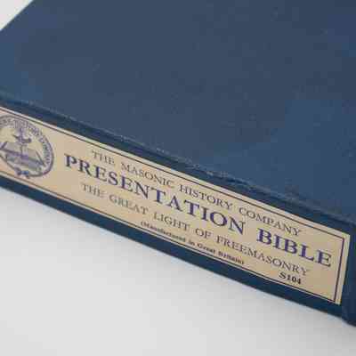 Box of the Masonic Presentation Bible given to Mrs. Jessie Jordan at a Ladies' Festival.: Up close image of the end of the blue Presentation Bible box. The box reads "THE MASONIC HISTORY COMPANY PRESENTATION BIBLE THE GREAT LIGHT OF FREEMASONRY" and "(Manufactured in Great Britain) S104." There is also a Masonic emblem to the left with the bible in view.