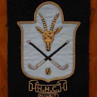 Field Hockey Plaque Close-up: A blue plaque embroidered onto felt with a goat head, field hockey sticks and a ball. Underneath is a ribbon with "H.H.C" and "Kuwait."