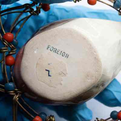 Bottom of ceramic bird: Unglazed bottom of the bird. It has paper-like residue from what was likely a label. All it says is "FOREIGN" in blue ink.