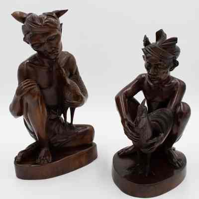 Pair of carved wooden figurines from Bali.: Image of the pair of carved wooden seated cockfighters with cock figurines.