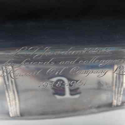 Engraving on the silver box containing to the book with the signatures from the employees of the Kuwait Oil Company.: Up close image of the engraving on the top of the silver pedestal box. It is engraved with "L.T. Jordan K.B.E. from his friends and colleagues in the Kuwait Oil Company Ltd. 1918-1961."