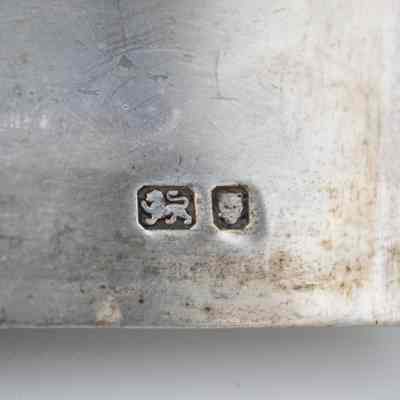Silversmith marks on the bottom of the silver casket humidor.: Up close image of the silversmith marks on the silver casket humidor. One mark is the lion passant, indicating the piece is genuine silver. The other mark is a lion's head, meaning the piece was made in London.