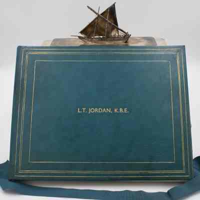 Book with signatures of employees from the Kuwait Oil Company.: Image of the blue leather book with gold detailing printed with "L.T. Jordan, K.B.E."
