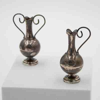 Miniature silver handled vases.: Up close image of the pair of miniature silver handled vases with round base and flared lip. The one on the right is missing its left handle.