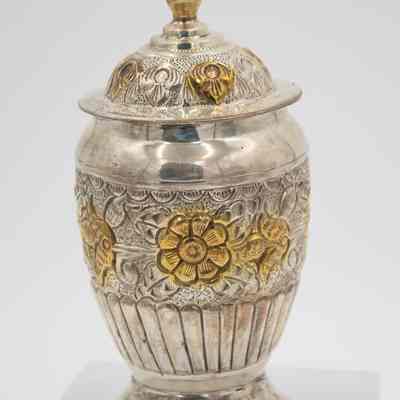 Small urn-shaped sugar jar given to Mrs. Jessie Jordan by Mrs. Al-Ghanim.: Up close image of the small engraved silver urn-shaped sugar jar decorated with yellow gold roses and a pointed lid.