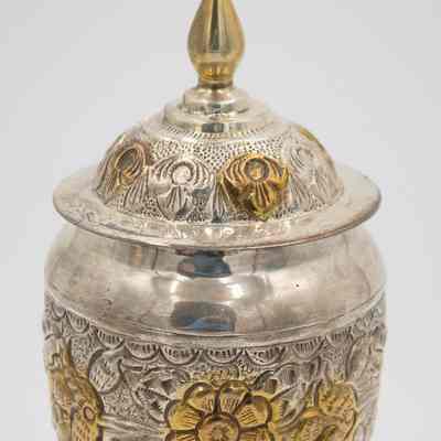 Body of small urn-shaped sugar jar given to Mrs. Jessie Jordan by Mrs. Al-Ghanim.: Up close image of the body of the small engraved silver urn-shaped sugar jar decorated with yellow gold roses and a pointed lid.
