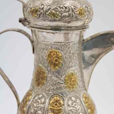 Body of coffee pot given to Mrs. Jessie Jordan by Mrs. Al-Ghanim.: Up close image of the body of the engraved silver coffee pot decorated with yellow gold roses.