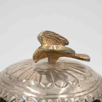 Falcon on top of the incense burner given to Mrs. Jessie Jordan by Mrs. Al-Ghanim.: Up close image of the gold cast falcon on the top of the silver incense burner. The wings are engraved with feather details. There is an engraved flower design under the falcon.