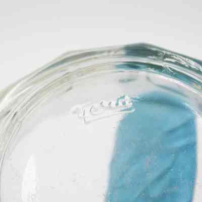 Bottom of clear glass dish found inside the incense burner.: Up close image of the bottom of a clear glass dish. It is imprinted with a small word that is illegible.
