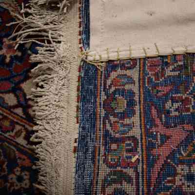 Red and blue area rug: The image shows a detailed view of the backside of an intricately patterned, red and blue woven rug's edge.