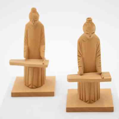Pair of carved wooden figurines of men playing instruments.: Up close image of two carved wooden figurines of men playing the Chinese zither. They are carved from light brown cedar wood.