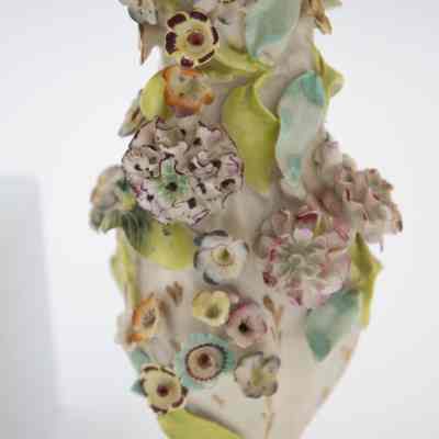 Details on the porcelain bud vases.: Up close image of one of the two porcelain vases decorated with pastel hand-painted encrusted flowers. The flowers are pink, blue, purple, red, and orange with green leaves. There is also gold foil detail around the edges of the vase and throughout the piece.