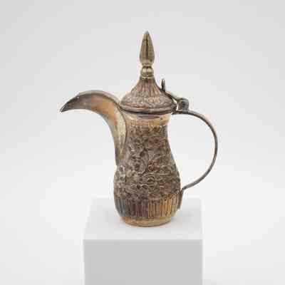 The larger coffee pot from the coffee service given to the Jordans by Sheikh Ahmad Al-Jaber Al-Sabah.: Image of the silver debossed coffee pot decorated with vines and flowers and a pointed lid.