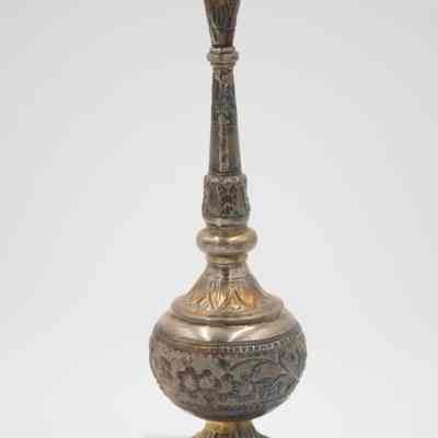 Rose water sprinkler from the coffee service given to the Jordans by Sheikh Ahmad Al-Jaber Al-Sabah.: Up close image of the silver rose water sprinkler decorated with debossed flowers, leaves, and vines. The gold detail on the leaves is faded.
